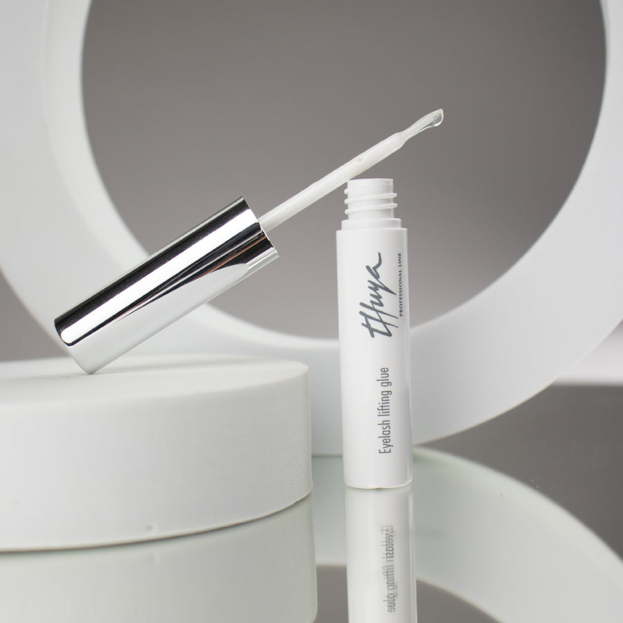 "Thuya Eyelash Lifting Glue, clear adhesive for securing lashes during lifts, ensuring strong hold and long-lasting results. small white tube with silver lid, Brush attached to the lid "